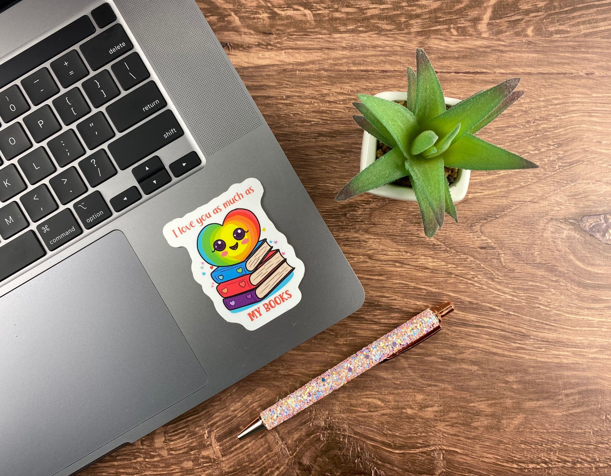 Sticker with a rainbow colored heart on a stack of books that says I love you as much as my books, displayed on a laptop